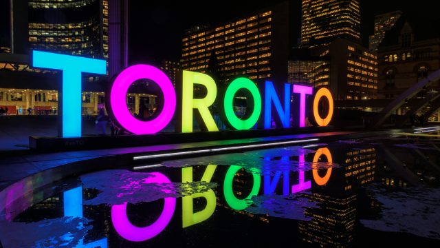 View of Toronto Sign on Nathan Phillips Square at night, in Toronto, Canada. Illuminated City Hall and the Freedom Arches in background.