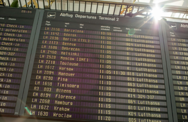 Departure board at an airport displaying flight information, including destinations, times, and airlines, with the current time shown.