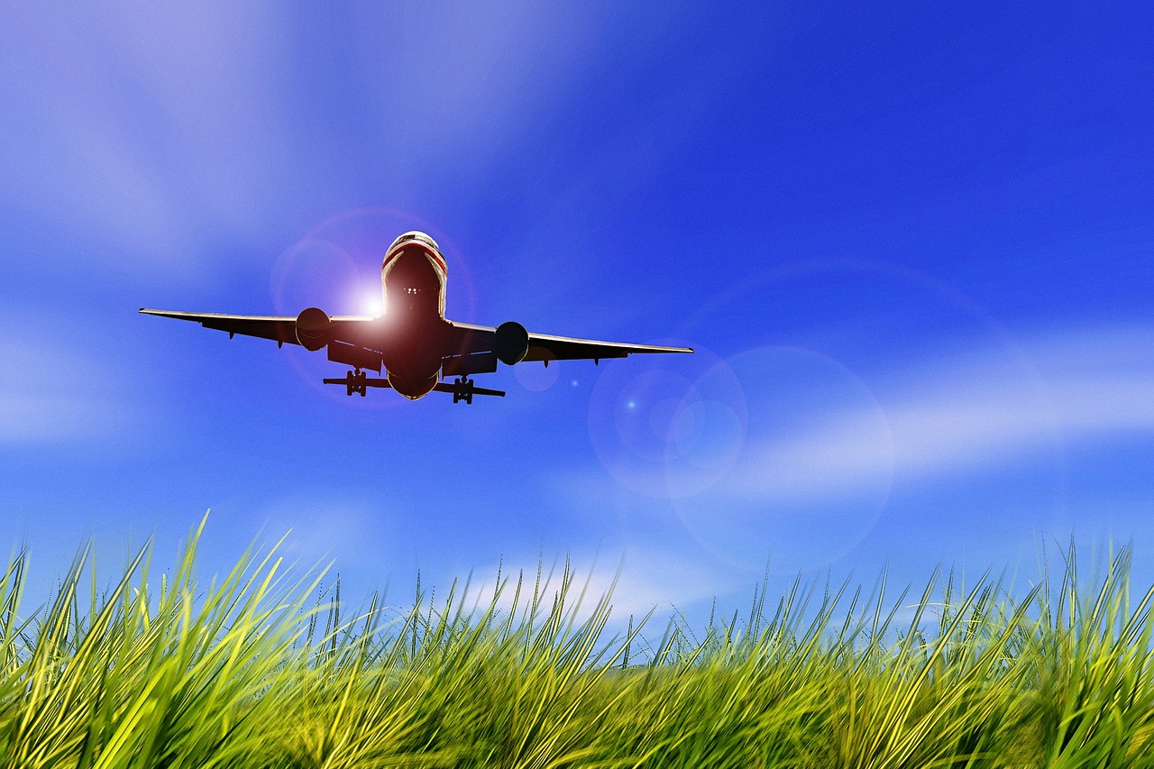 Airplane flying low over a grassy field under a clear blue sky, with sunlight creating a lens flare effect, conveying freedom and adventure.