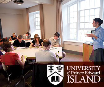 A teacher at the front of a classroom speaking to a group of students seated around shared desk tables at the University of Prince Edward Island in Canada.