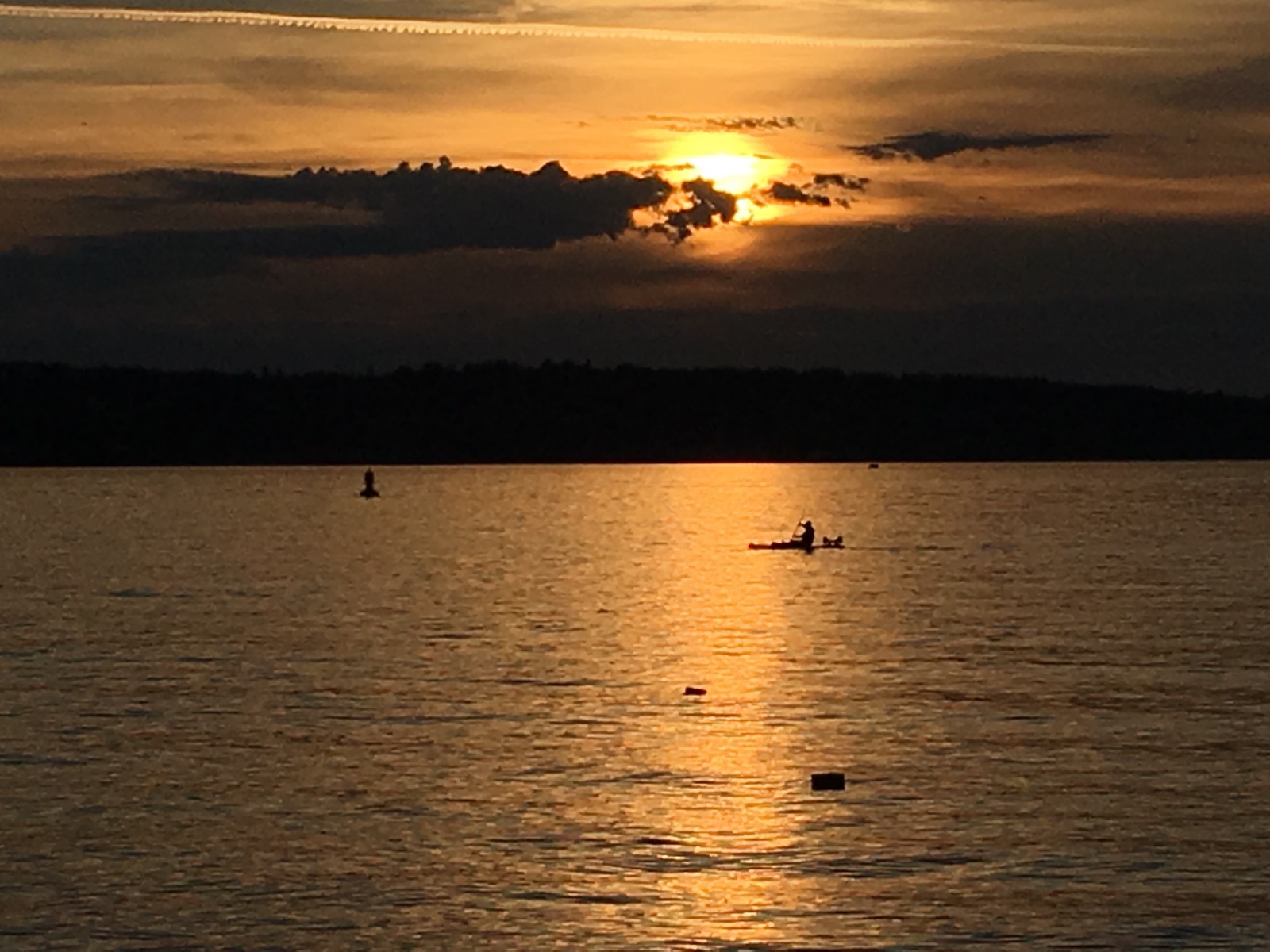 Sunset over a calm lake with silhouettes of a kayaker and a paddleboarder, golden reflections on the water, and an orange-hued sky.