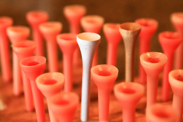 Close-up of a cluster of red plastic golf tees with one white wooden tee in the center, creating contrast and focus. Warm and vibrant tone.