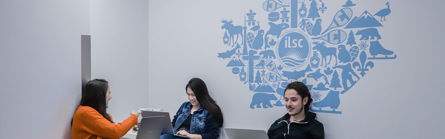 Two female and one male student in the Montreal student lounge in front of an ILSC Canada Maple Leaf graphic.  See our college program start dates in Canada