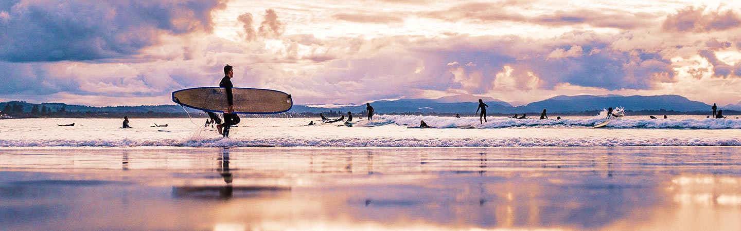 Student life in Australia - beach full of surfers with man carrying surfboard at the front - student safety, cost of living, work rights and more in Australia