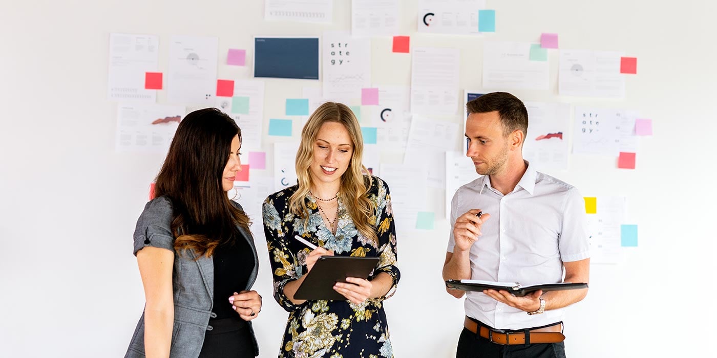 Three colleagues (two women and one man) discussing ideas with a white board in the background with coloured sticky notes. Take digital marketing programs at a career college in Canada in Vancouver, Toronto or Montreal