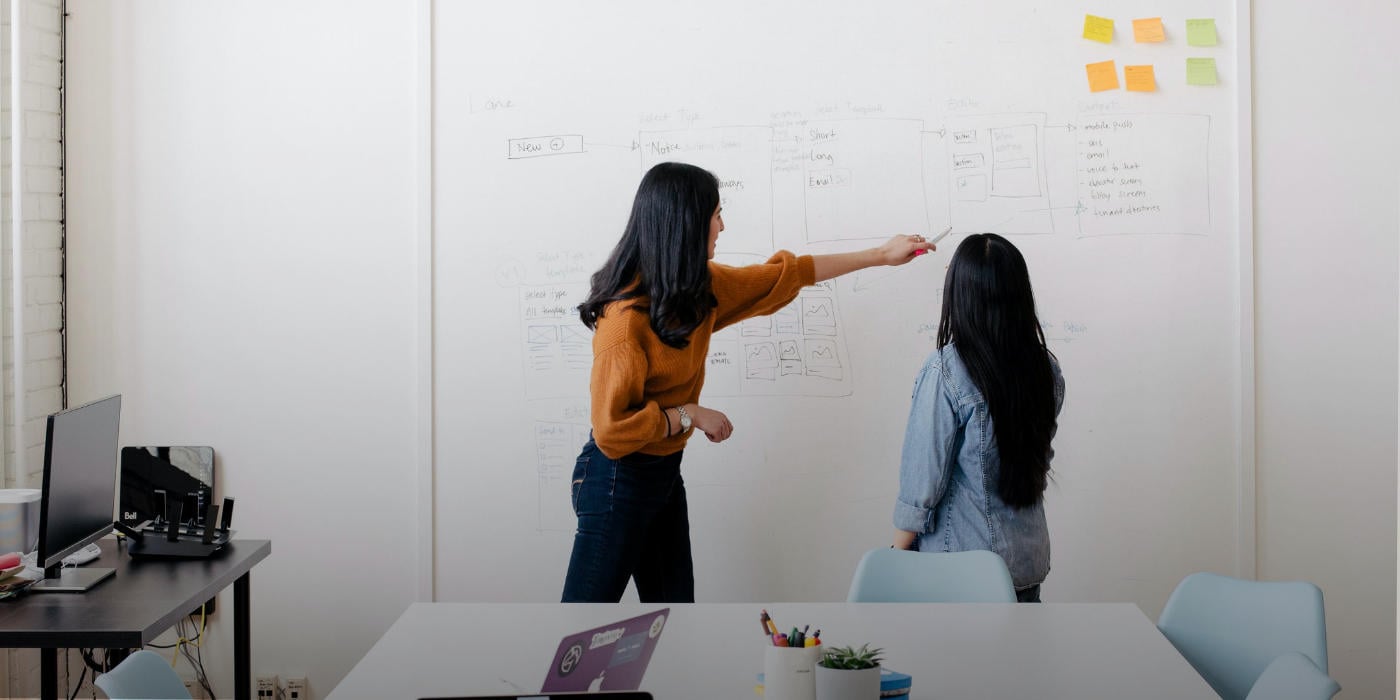 Two women colleagues with one pointing out things to the other on a white board with notes - study leadership and innovation in Australia