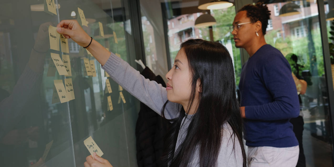 Two colleagues, one female and one male, add sticky notes to whiteboard highlighting tasks in Q1, Q2, Q3, and Q4 -study Program Management in Australia