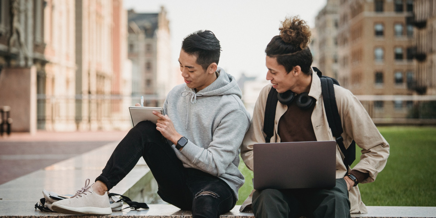 Two male international students with a computer and notebook outside on university campus.  Take a transfer credit program and get advanced standing in a bachelor's degree program in Canada.