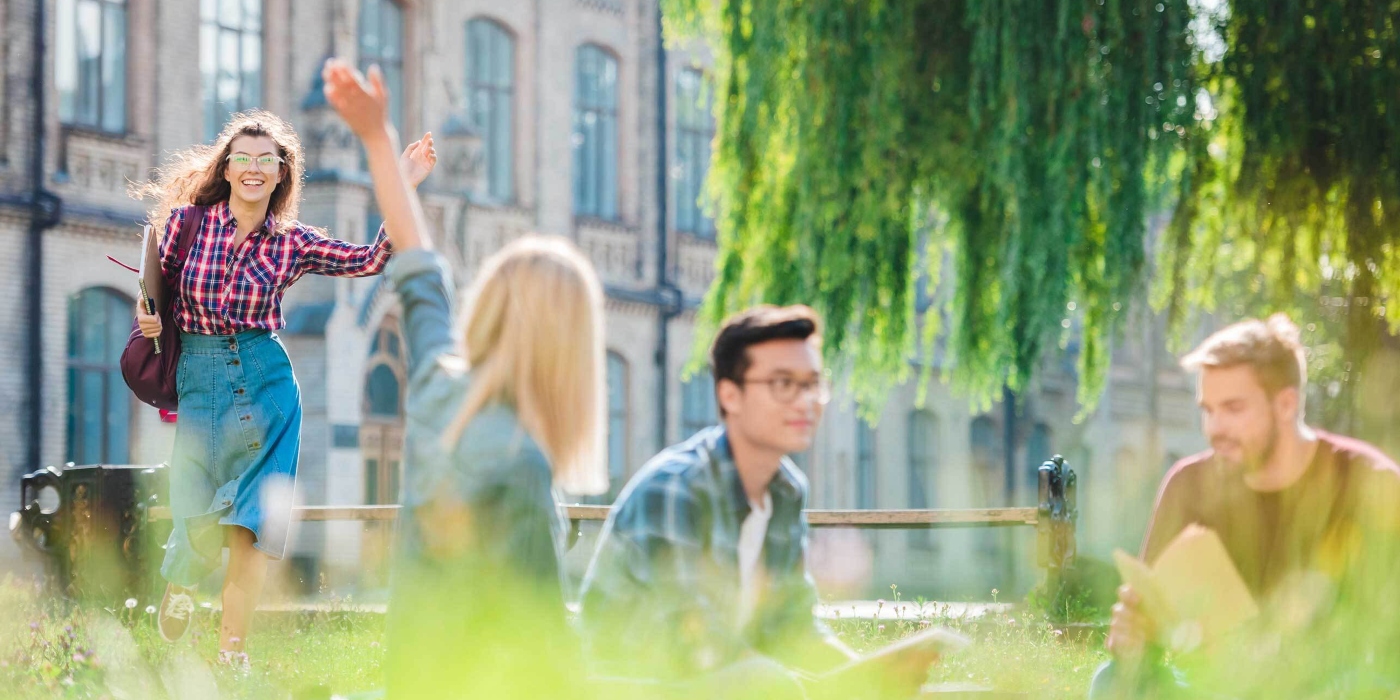 Students in the grass waving to each other in front of a university - take a credit transfer program at Greystone College Australia and earn credits that are accepted for advanced standing at partner colleges and universities