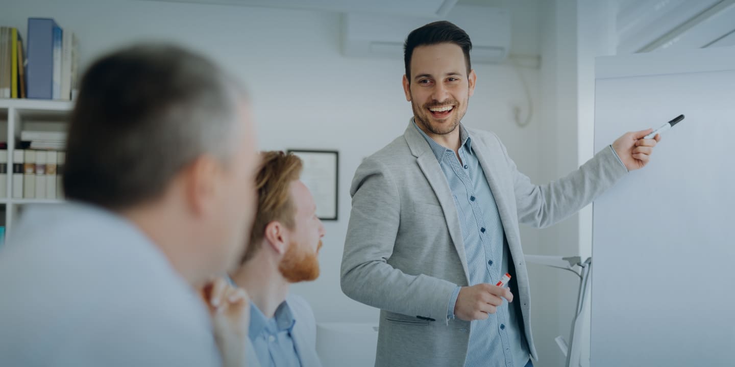 studying at Greystone College Australia.  Standing white male in suite points out something on white board to two seated white male colleagues - study in Australia at a career college / vet college