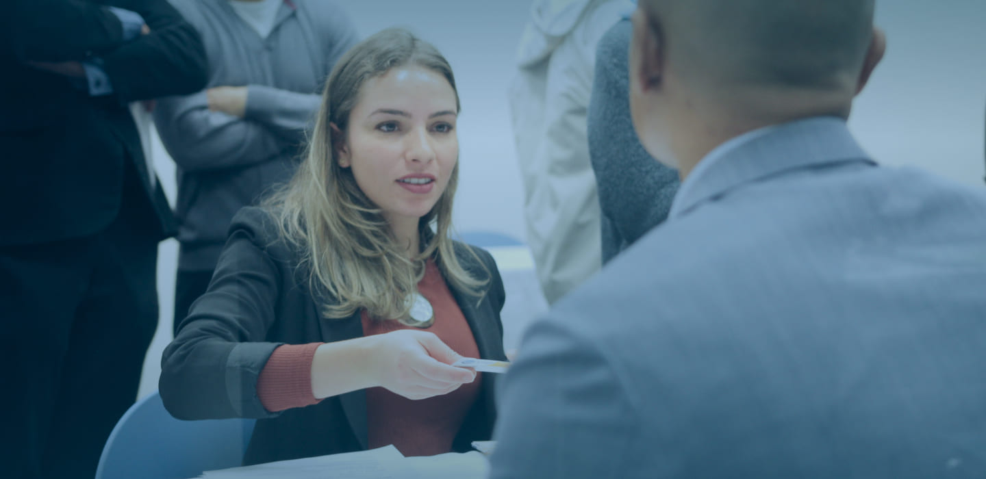 Female student dressed in blazer at a Greystone College career fair talking with a potential employer. Small and large businesses hire a co-op student to support your business. Our students study business, hospitality, and digital marketing.